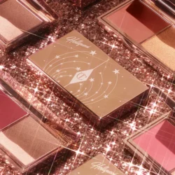 035_220006_HOLIDAY_SL_HOLLYWOOD_BLUSH_GLOW_V1_Square_1000x1000_RGB__1_jpg - shopcosmoprof.com Close-up of pink makeup palettes on a glittery surface, with a central compact featuring a starry circular design and 'Hollywood' branding.