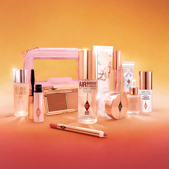Assorted pink-and-gold makeup products arranged on a peach background, including a compact, bottles, and brushes.