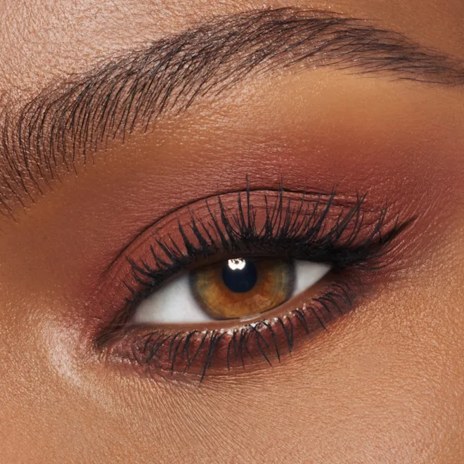 Close-up of a brown eye with warm copper-orange eyeshadow, black eyeliner, and long curled lashes.
