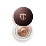 Bronze-cream eyeshadow in an open circular jar with a dark brown lid bearing a gold CT/CT logo, showing metallic product inside.