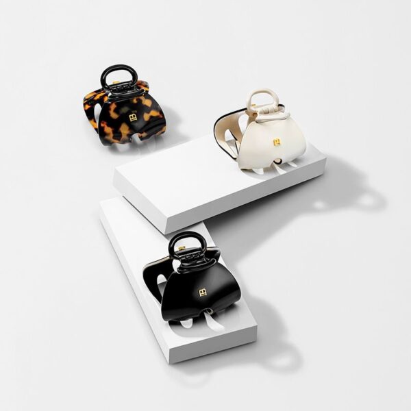 Three fashionable handbags in tortoiseshell, ivory, and black, arranged on white display blocks against a light background.