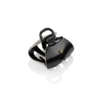 Black glossy, handbag-style accessory with a curved handle and gold JB logo on a white reflective surface.