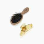 Beige Balmain Paris oval hair brush with black bristles next to a pale marbled hair clip