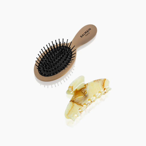 Beige Balmain Paris oval hair brush with black bristles next to a pale marbled hair clip