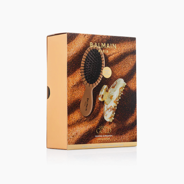 Balmain Paris hair styling set box with a black round brush and gold-toned styling tool against a sandy gold background (retail packaging)