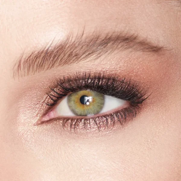 Close-up of a green hazel eye with pink shimmery eyeshadow, black eyeliner, and long lashes, with a groomed eyebrow above.