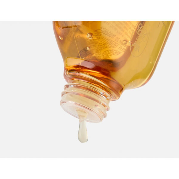 Amber glass bottle tilted, pouring a thin stream of golden liquid with a drop nearing the spout.
