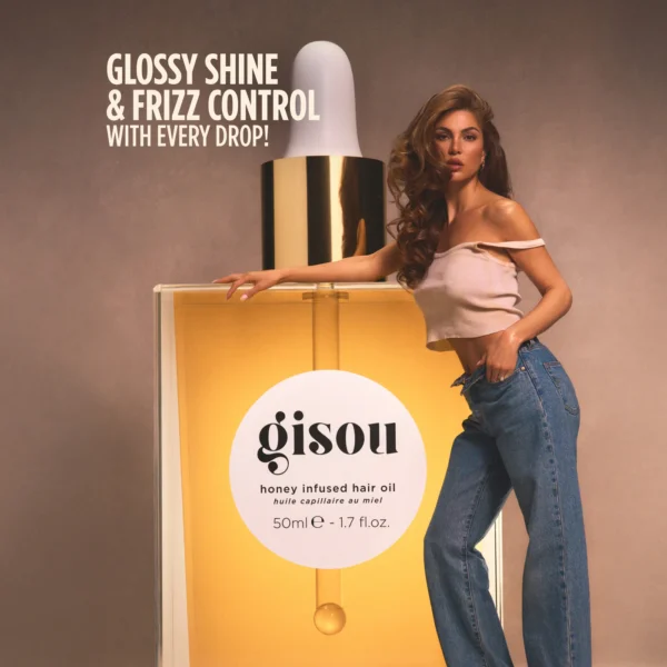 Model leaning on a giant Gisou honey-infused hair oil bottle, promoting glossy shine and frizz control in an ad image.