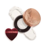 Charlotte Tilbury compact with rose-gold lid, white pressed powder, and a burgundy heart-shaped puff beside it.