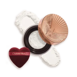 Charlotte Tilbury compact with rose-gold lid, white pressed powder, and a burgundy heart-shaped puff beside it.