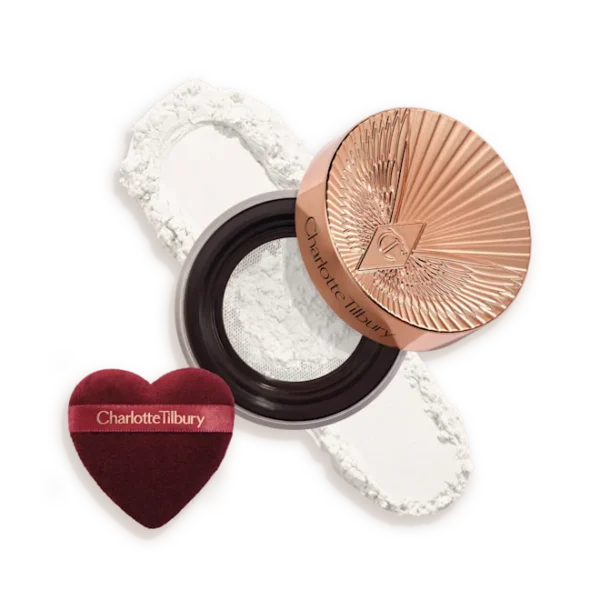 Charlotte Tilbury compact with rose-gold lid, white pressed powder, and a burgundy heart-shaped puff beside it.