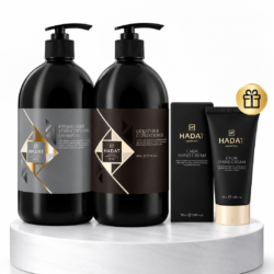 Set of black Hadat shampoo, conditioner bottles and hand cream tubes on a marble pedestal, with a small gift badge.
