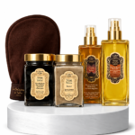 Luxurious spa gift set on a white marble pedestal: two gold spray bottles, two cream jars with gold lids, and a brown exfoliating mitt in the background.