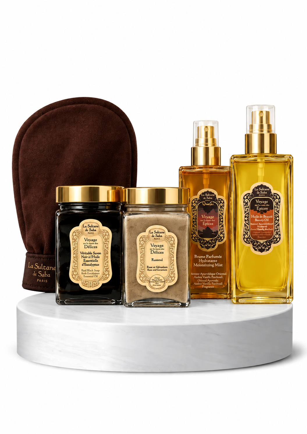 LA SULTANE DE SABA RYTŲ PRABANGOS RITUALAS - shopcosmoprof.com Luxurious spa gift set on a white marble pedestal: two gold spray bottles, two cream jars with gold lids, and a brown exfoliating mitt in the background.