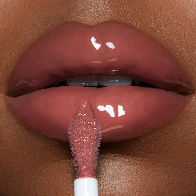 Close-up of glossy pink lips with a lip gloss wand applying product to the lower lip.