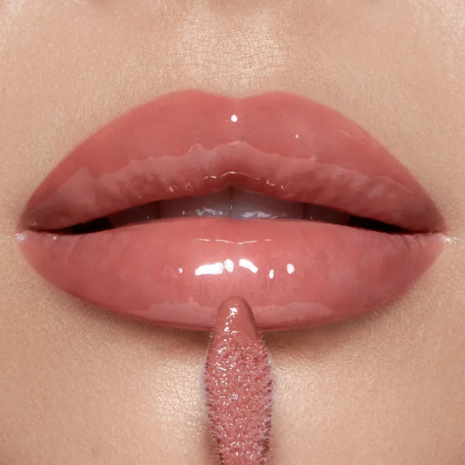 Close-up of glossy pink lips with a lip gloss wand touching the lower lip, about to apply makeup.