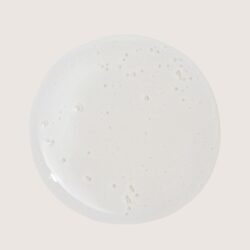 Top-down view of a frothy white liquid filling a circular surface on a pale beige background (milk foam).