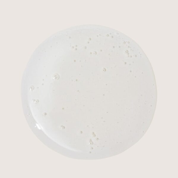 Top-down view of a frothy white liquid filling a circular surface on a pale beige background (milk foam).