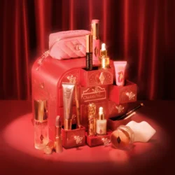 251027_Holiday-26_sl_CD_260604_Advent_Calendar_R9_1000x1000jpg - shopcosmoprof.com Assorted pink and gold makeup products arranged on stacked decorative boxes with a pink quilted bag in the background.
