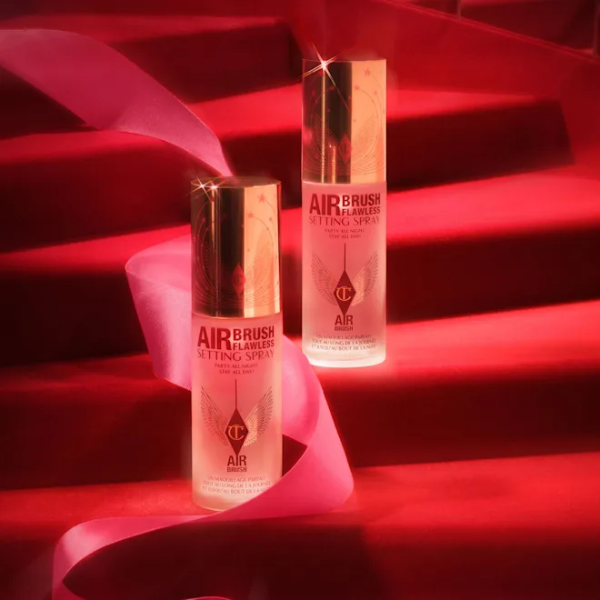 Two Airbrush Flawless Setting Spray bottles on a red-lit staircase with pink ribbon, promoting makeup setting spray.