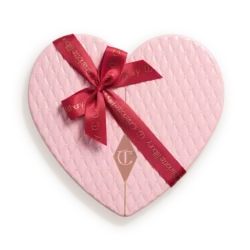Heart-shaped pink quilted gift box tied with a red ribbon bow and tag showing a brand logo