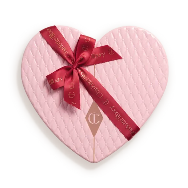 Heart-shaped pink quilted gift box tied with a red ribbon bow and tag showing a brand logo