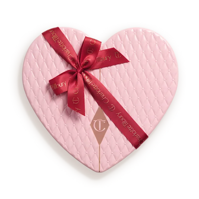 Packshot_of_Box__PILLOW_TALK_ICONS_ON_THE_GOpng - shopcosmoprof.com Heart-shaped pink quilted gift box tied with a red ribbon bow and tag showing a brand logo