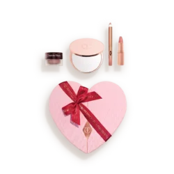 Heart-shaped pink makeup gift set in a light case, showing a quilted blush with a red ribbon and accompanying powders and lip products.