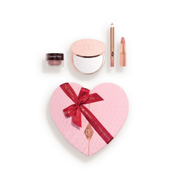 Heart-shaped pink makeup gift set in a light case, showing a quilted blush with a red ribbon and accompanying powders and lip products.