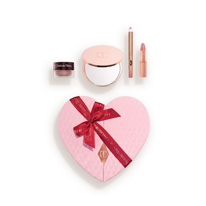 Heart-shaped pink makeup gift set in a light case, showing a quilted blush with a red ribbon and accompanying powders and lip products.