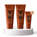 Three orange La Sultane de Saba body care tubes on a white marble pedestal with ornate labels and a small gift badge nearby.