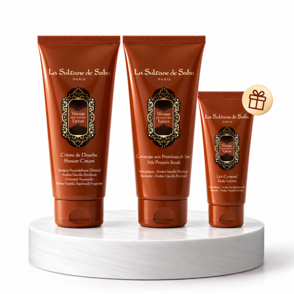 Three orange La Sultane de Saba body care tubes on a white marble pedestal with ornate labels and a small gift badge nearby.