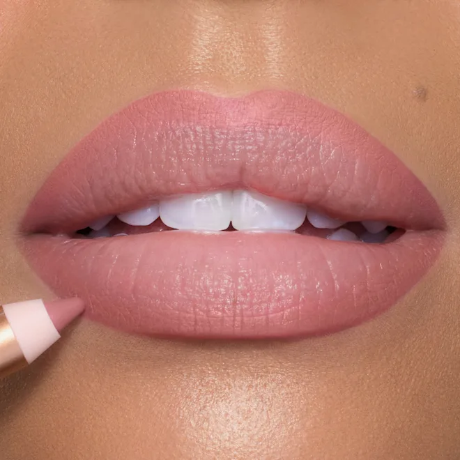 Close-up of glossy pink nude lips with a lip applicator resting at the corner, showing a pink lipstick being applied.